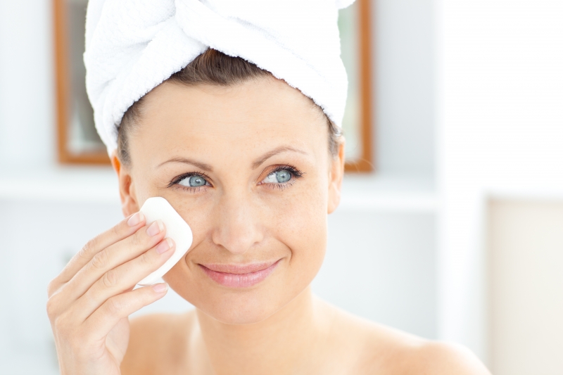 young-woman-putting-cream-on-her-face-wearing-a-towel-in-the-bathroom